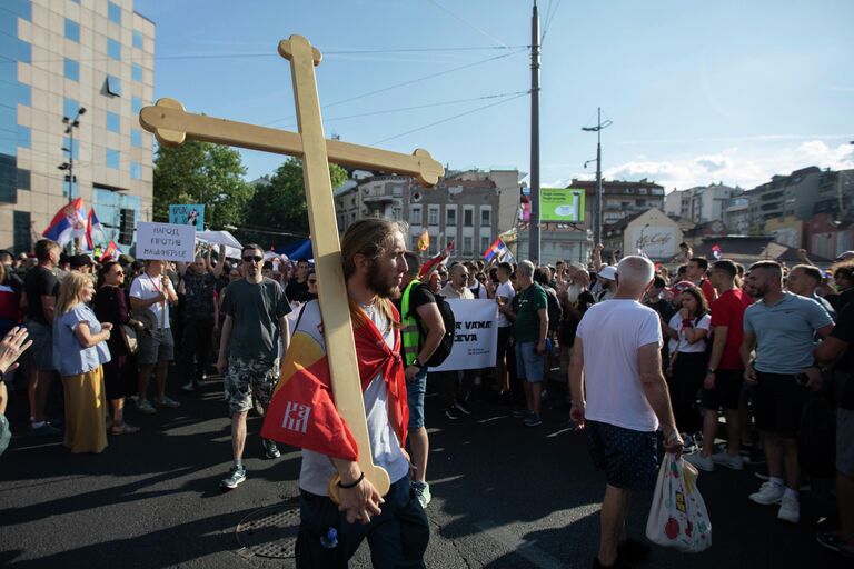 Молодой человек несет деревянный крест на плече на площади Славия в Белграде во время акции протеста